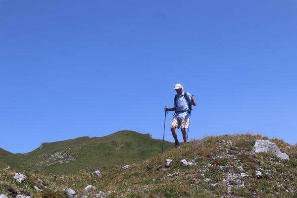A lone hiker is captured mid-stride, ascending a grassy, rocky hill under a vast, clear blue sky